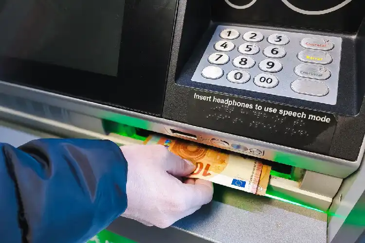 Jovem segurando notas de dinheiro em caixa eletrônico