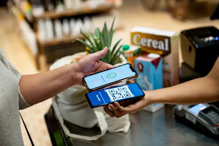 Pagamento por aproximação com dois celulares em um supermercado, um exibindo um QR Code e o outro confirmando a transação com Nomad ou BS2