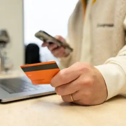 Homem segurando um cartão de débito internacional e usando o celular
