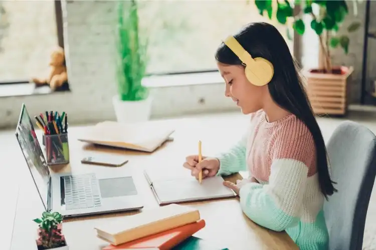 Criança estudando inglês online em escrivaninha com fone de ouvido rosa