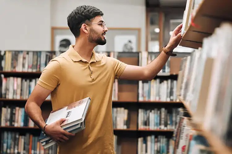 Homem procura livros em biblioteca de faculdade