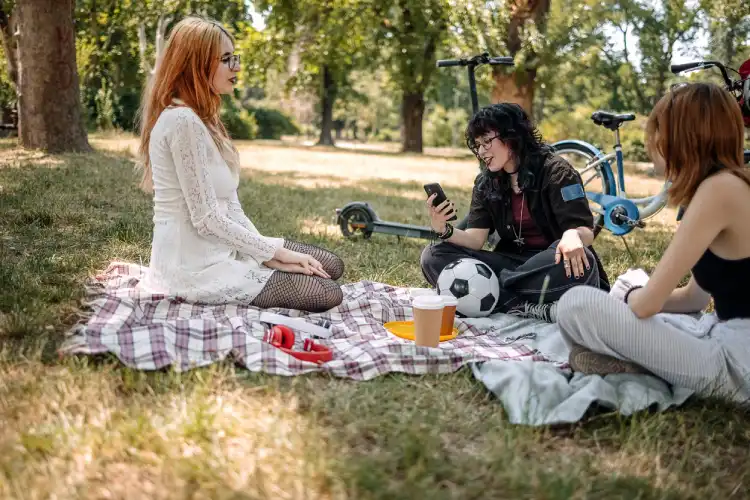 Três jovens fazendo piquenique em um parque na França, sorrindo e conversando.