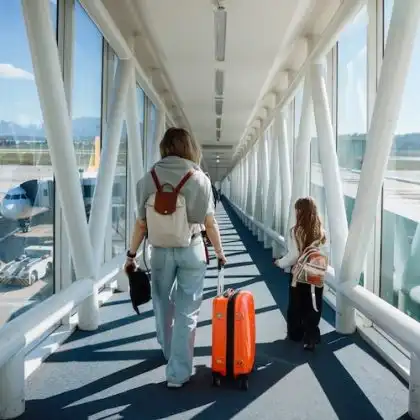 Passageiras caminham por uma ponte de embarque com destino ao avião, levando bagagens e mochilas.
