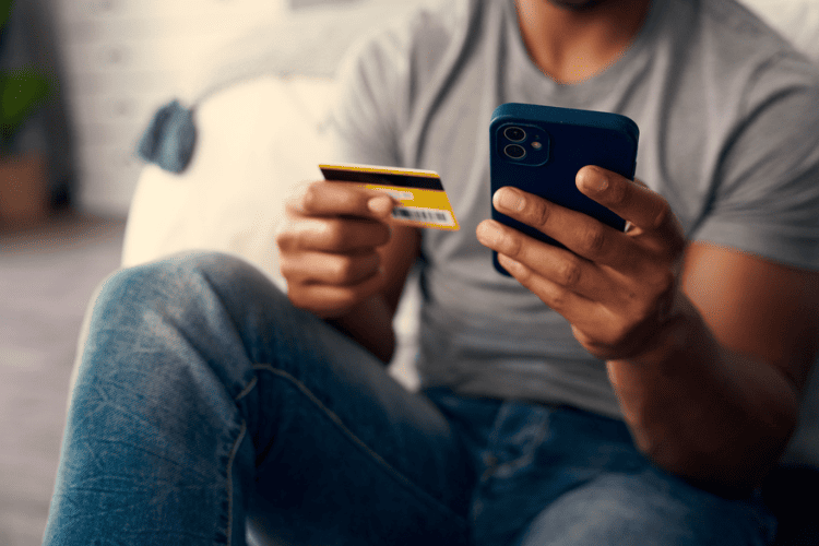 Pessoa sentada usa o celular enquanto segura um cartão de viagem internacional