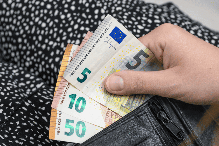 Pessoa segura notas de euro ao lado de uma bolsa