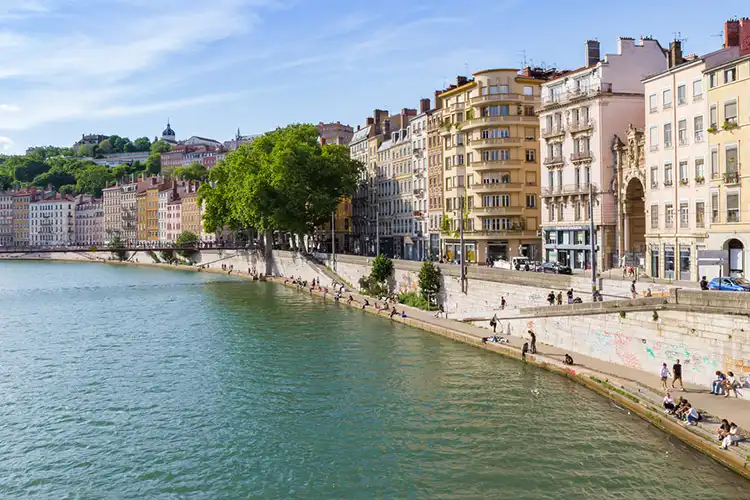 Cidade de Lyon, com pessoas sentadas à margem do rio Saône