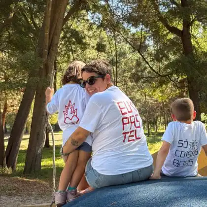 Mulher sentada com dois filhos em meio à natureza, olha para trás em direção à câmera.