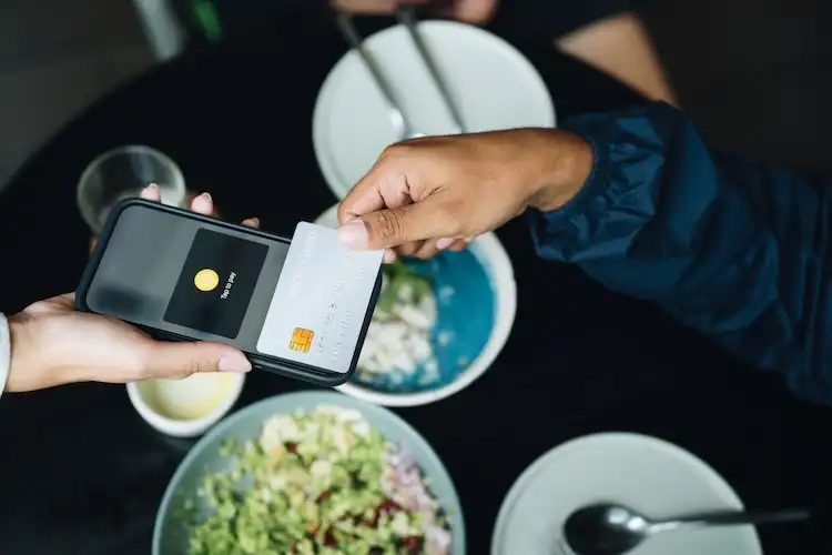 Pessoa realizando pagamento por aproximação com cartão em um restaurante.
