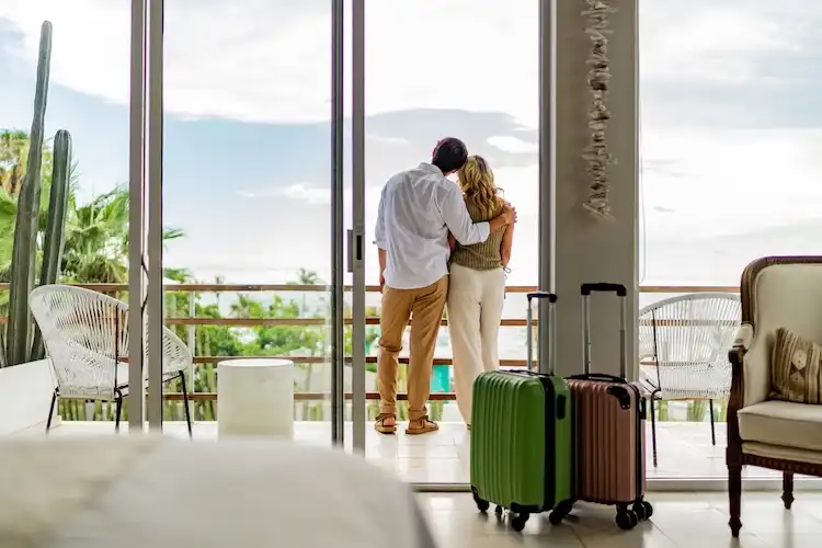 Casal de viajantes observa a paisagem, enquanto suas malas estão no quarto
