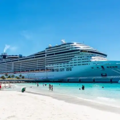 Navio de cruzeiro ancorado em uma praia de águas claras com turistas na areia