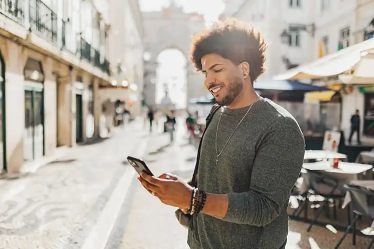 Homem sorri usando internet no celular em rua turística de Lisboa, Portugal