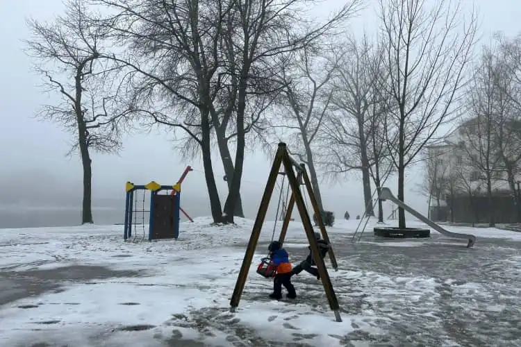 Duas crianças brincando em um parquinho em meio a neve e a neblina mostram como criar filhos entre duas pátrias pode ser desafiador