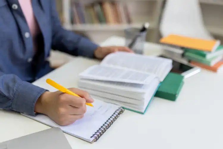 Estudante com livros e fazendo anotações no caderno.