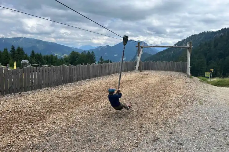 Criança se diverte no topo de uma montanha em uma paisagem com outras montanhas ao fundo, na Alemanha