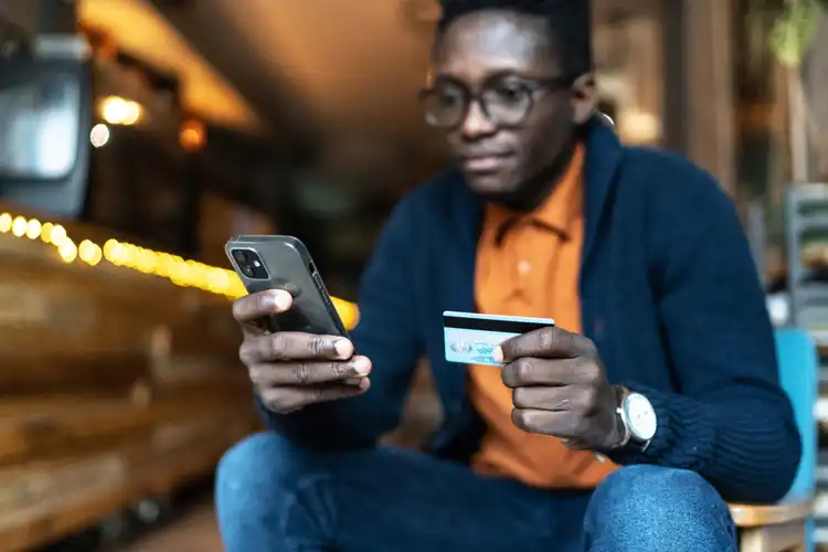Homem mexendo no celular com um cartão de banco