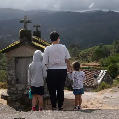 Mulher com duas crianças pequenas de mão dada com ela são vistos de costas observando a paisagem na aldeia Soajo