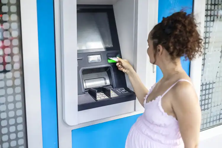 Mulher grávida sacando dinheiro da conta digital internacional em caixa eletrônico