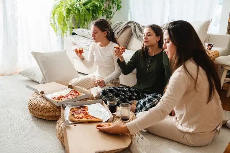 Amigas comendo pizza na sala de casa