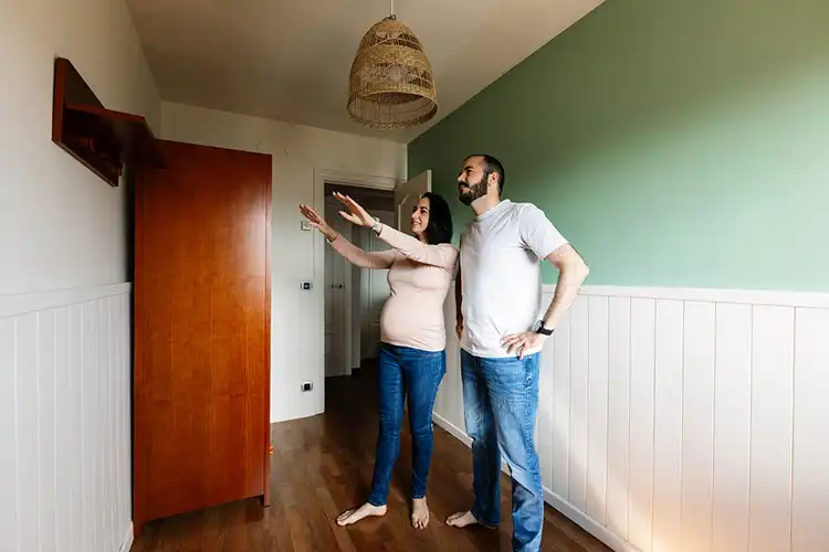 Mulher grávida e marido planejando arranjo de móveis para quarto de bebê