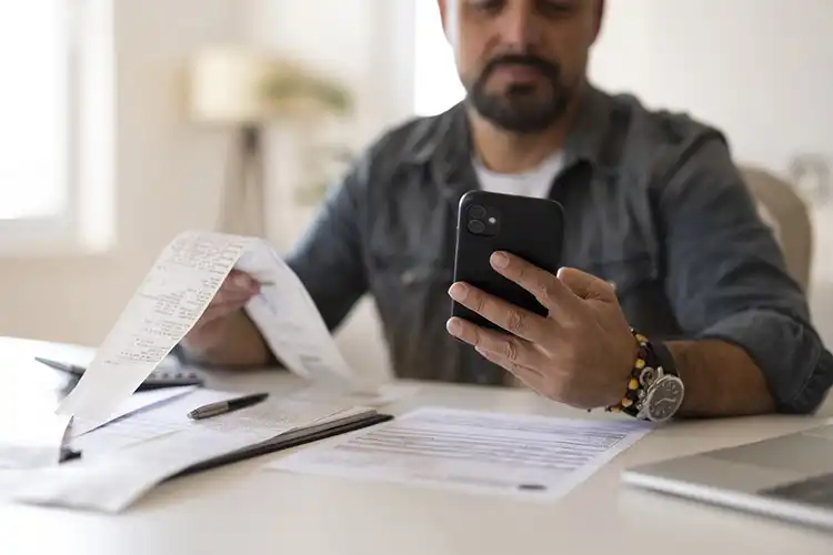 Homem fazendo contas usando o celular na sala de casa