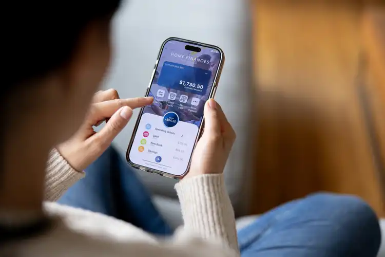 Mulher em casa usando um aplicativo financeiro no celular.