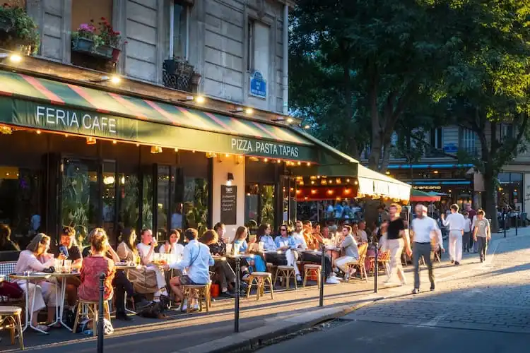 Pessoas jantam em mesas ao ar livre em café de rua em Paris.