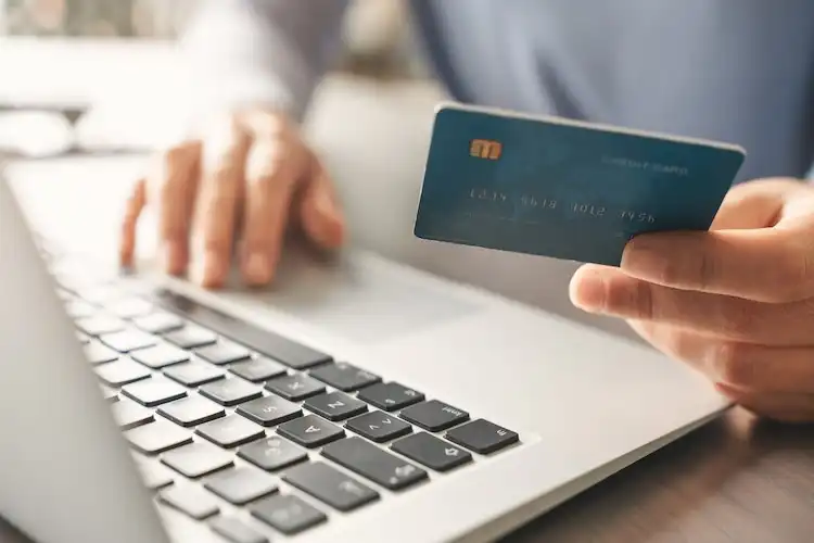 Pessoa utiliza cartão de crédito enquanto acessa computador para pagamento online.