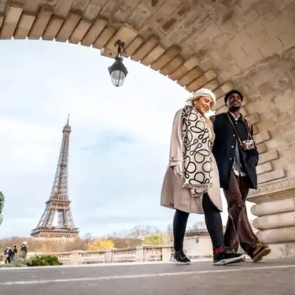 Casal caminha próximo à Torre Eiffel em Paris durante viagem.
