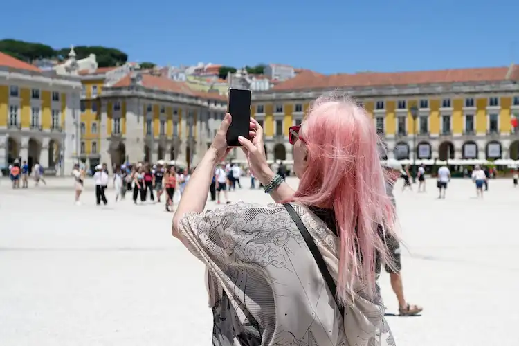 Mulher com seguro viagem Portugal fotografa praça turística em Lisboa