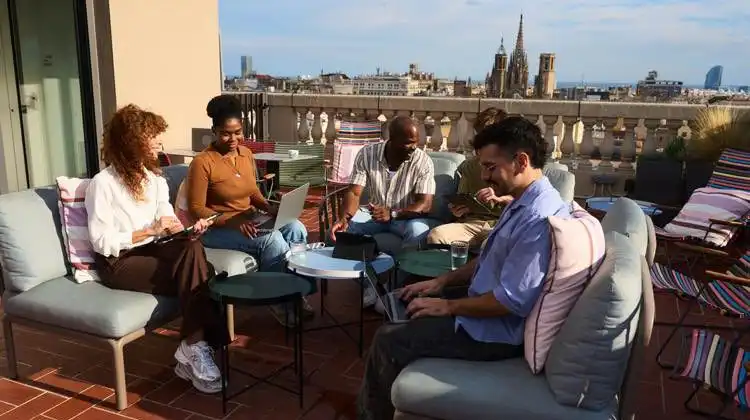 Grupo de nômades digitais conversa em terraço de prédio, em dia de sol