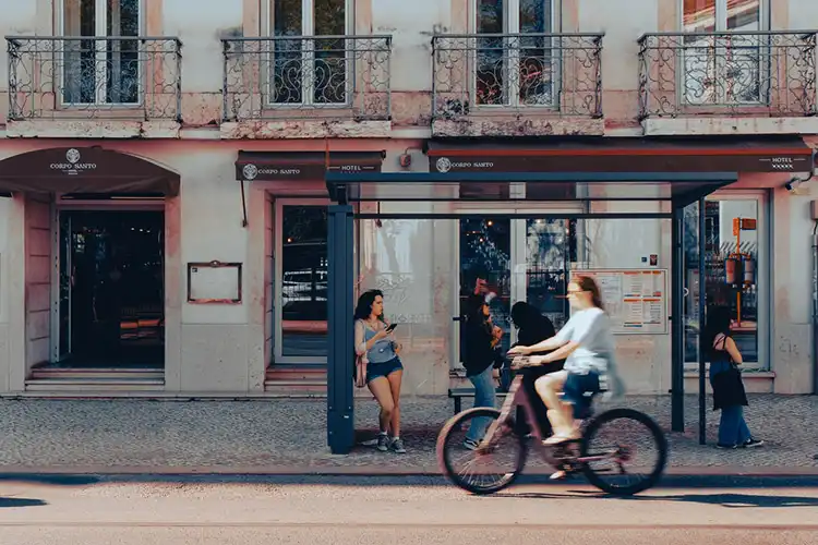 Pessoas no ponto de ônibus e movimento numa rua de Lisboa