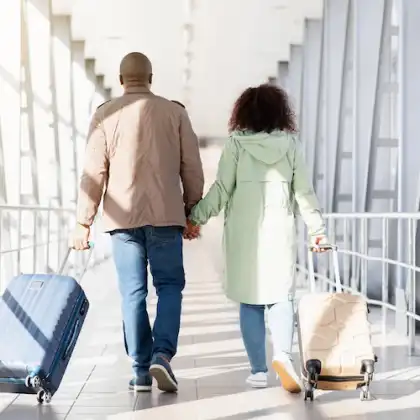Casal caminha com malas em corredor de embarque de aeroporto.
