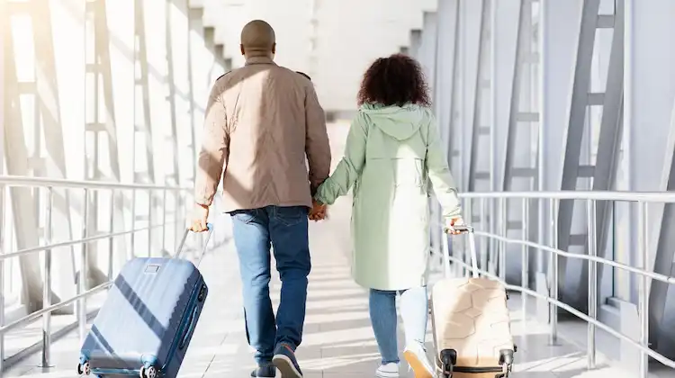 Casal caminha com malas em corredor de embarque de aeroporto.